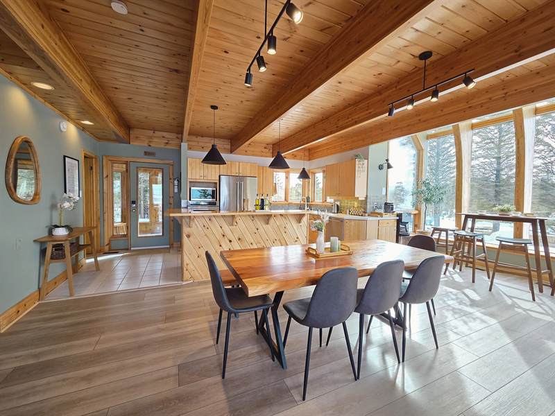 Dining area with live-edge wood table and grey chairs, pine ceilings, kitchen and window-side breakfast bar