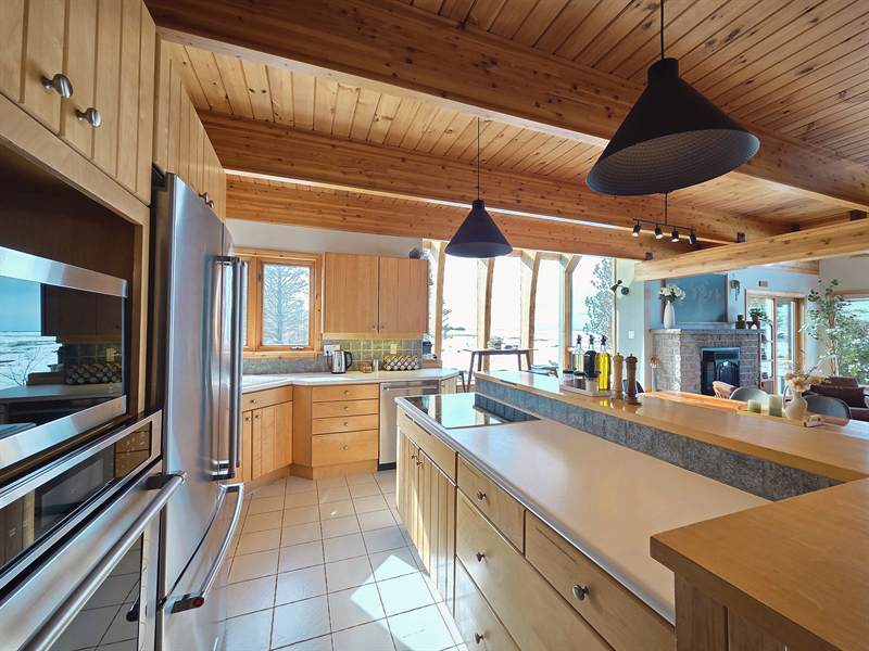 Kitchen with wood cabinets, stainless appliances, island cooktop and windows onto a snowy lakeshore