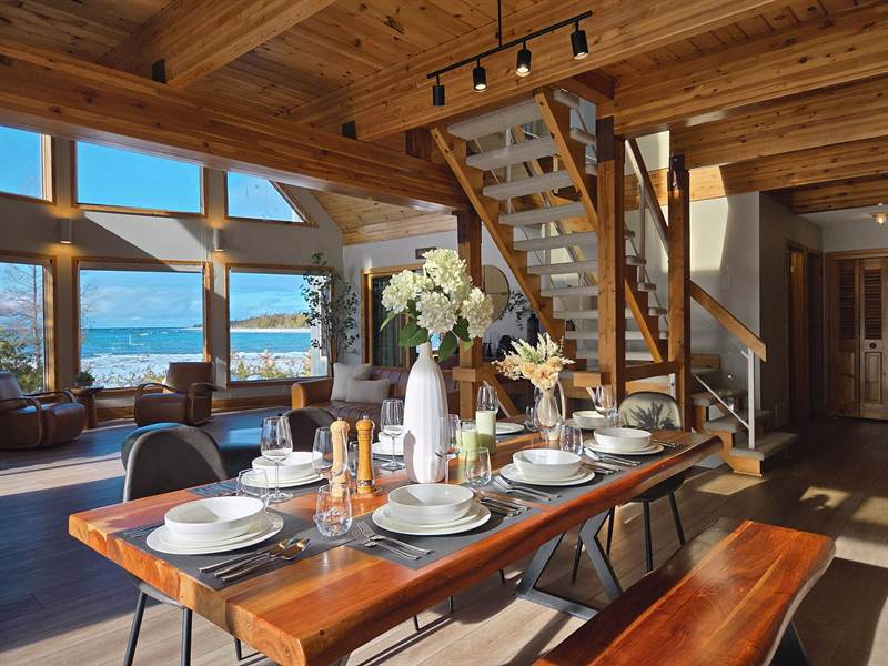 Dining table set with white dishes and wine glasses, staircase and lake-view windows behind