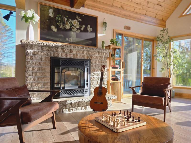 Stone fireplace with floral art above, guitar on stand, two armchairs and chess set on a round table