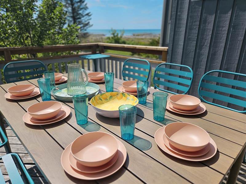 Deck table set with peach dishes, teal glasses and chairs, Lake Huron visible past the railing