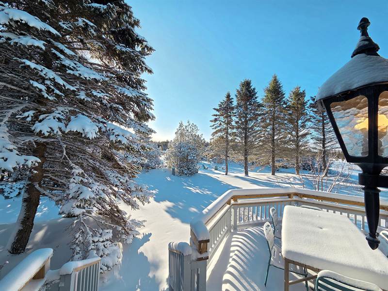 Snow-covered deck table, chairs and lantern with deep snow and snow-laden spruces beyond